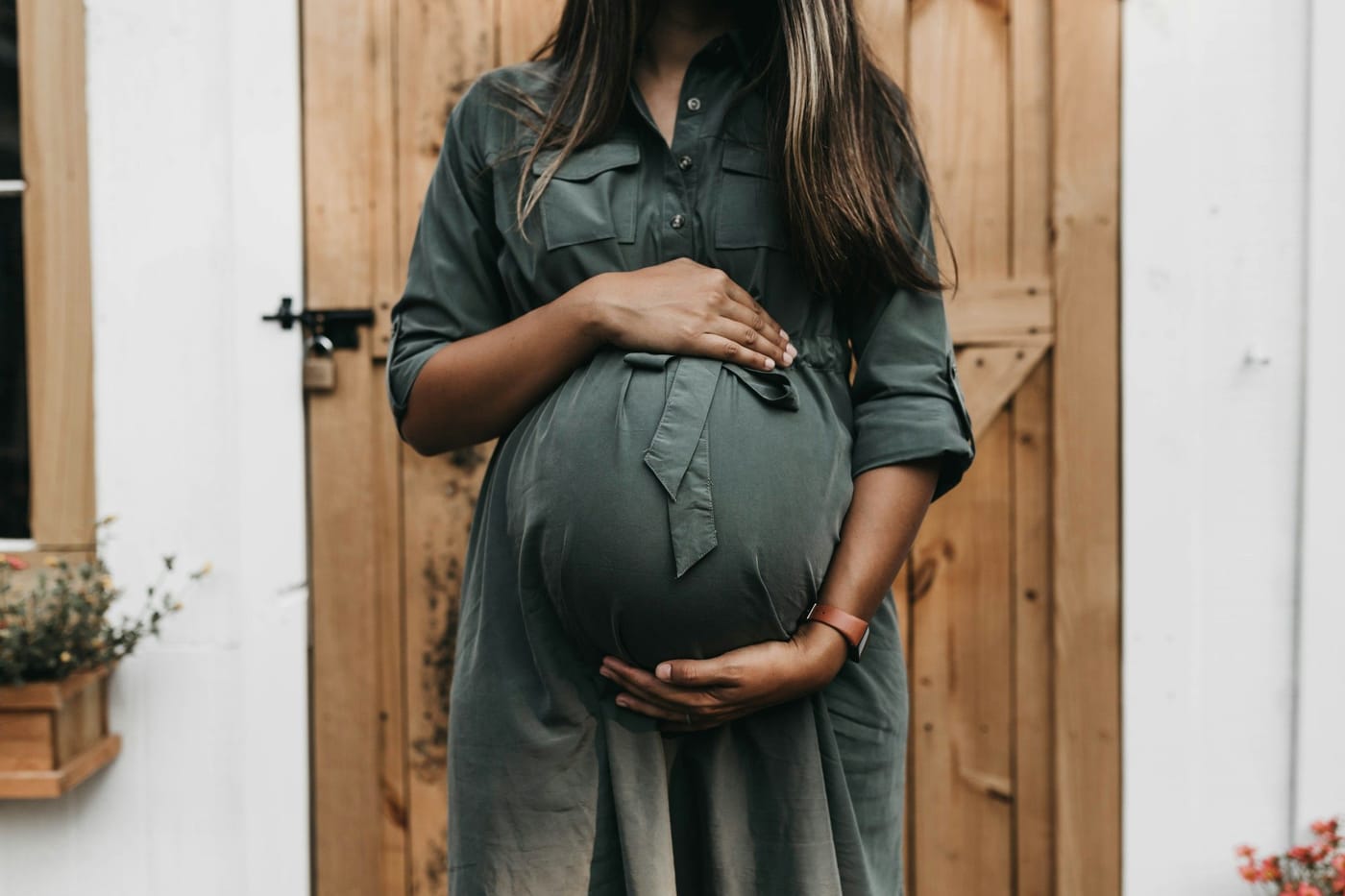 A pregnant woman in a green dress cradles her belly in front of a wooden door